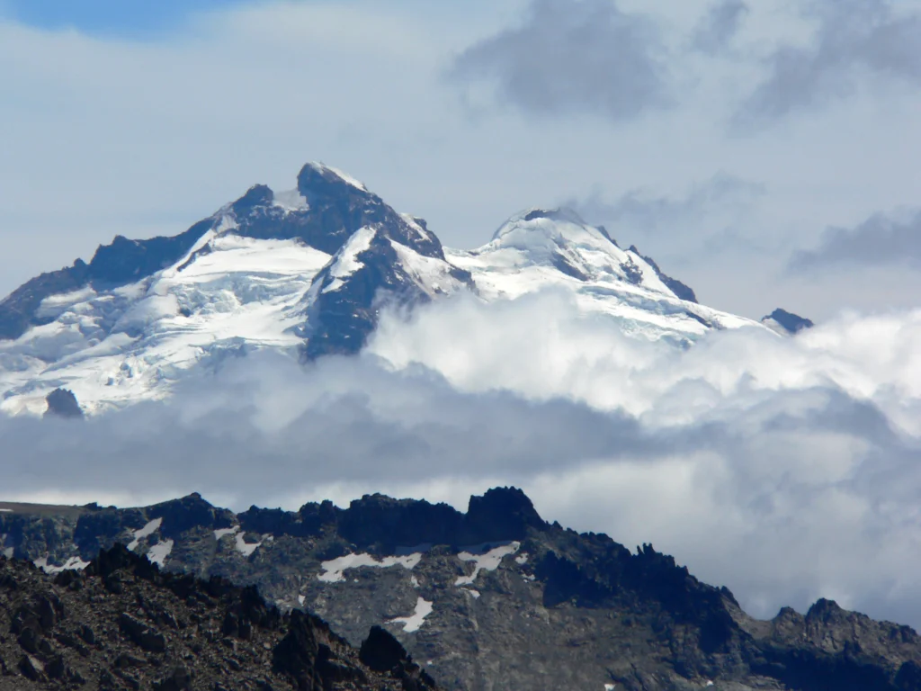 Cumbres nevadas del Cerro Tronador emergiendo entre nubes, con roca oscura en primer plano.