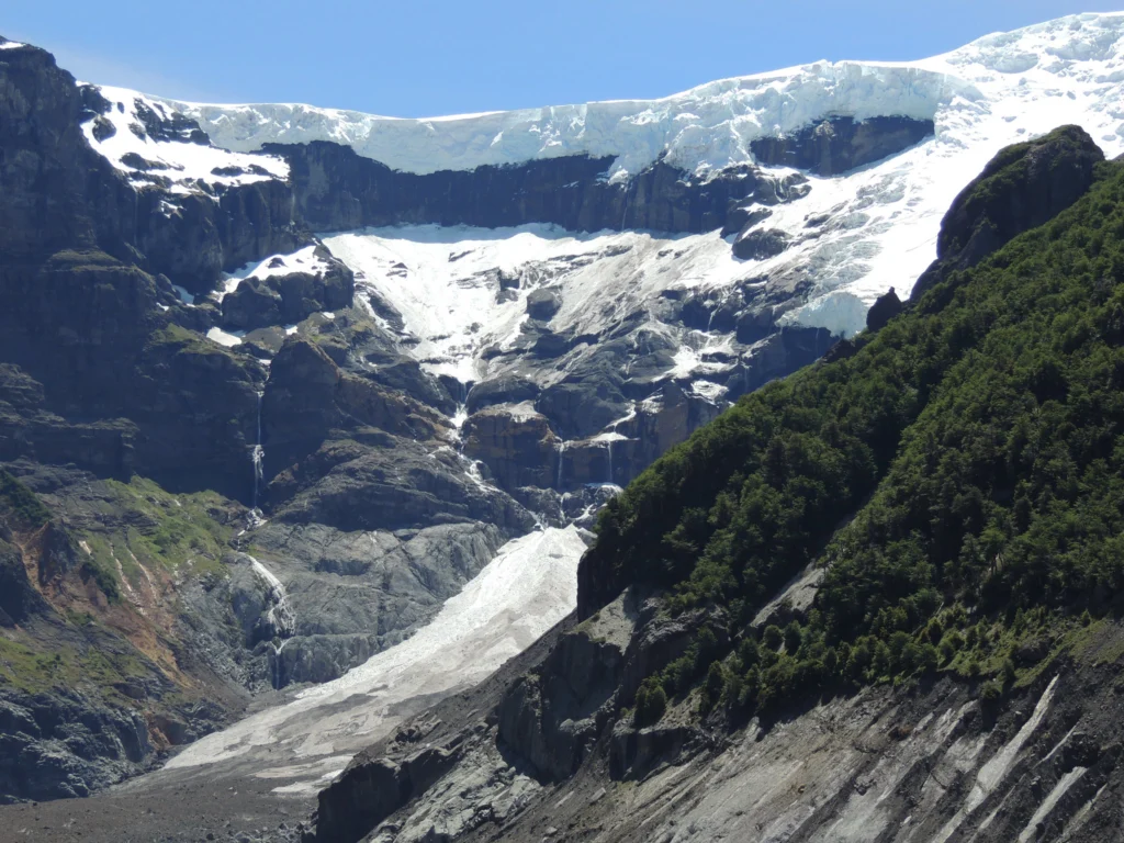 Glaciar colgante sobre paredes de roca con cascadas de deshielo cayendo al valle.