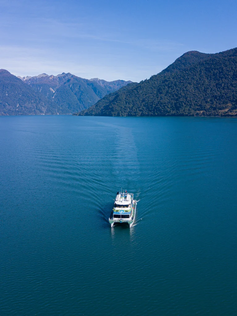 Catamarán navegando un lago de montaña rodeado de laderas boscosas, visto desde el aire.