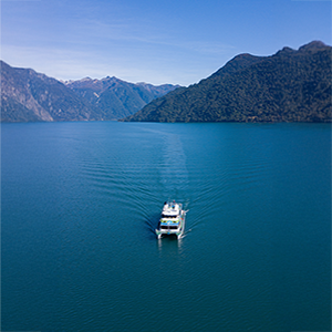 Catamarán navegando un lago de montaña rodeado de laderas boscosas, visto desde el aire.