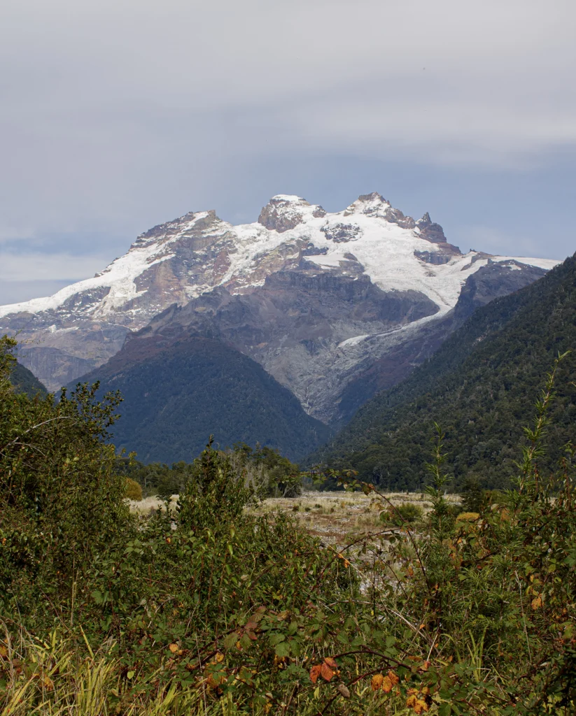 Cerro nevado con glaciares colgantes sobre el valle boscoso, en el tramo del cruce.