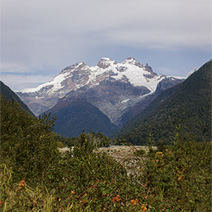 Cerro nevado con glaciares colgantes sobre el valle boscoso, en el tramo del cruce.