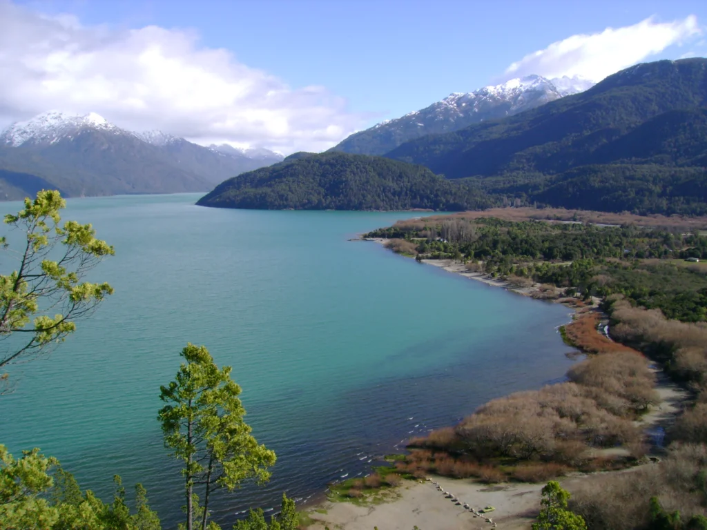 Aguas turquesas del Lago Puelo entre cerros boscosos y cumbres nevadas al fondo.