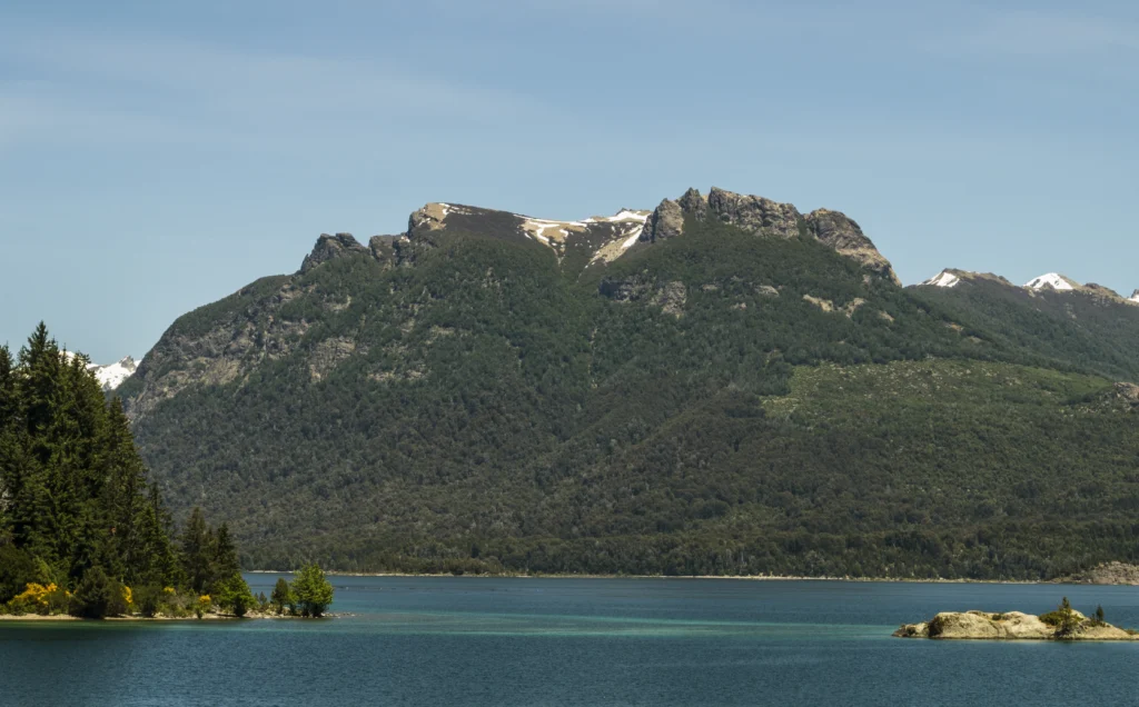 Wooded coast of Victoria Island on Nahuel Huapi Lake, with a chain of hills in the background.
