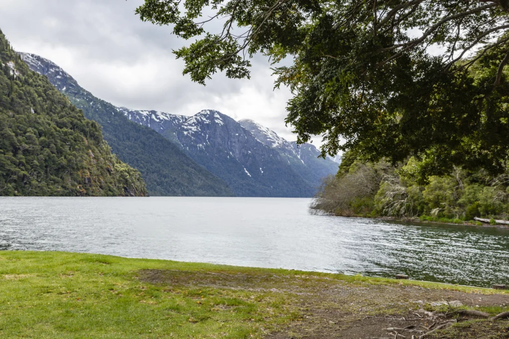 Orilla del Lago Frías encajonado entre laderas boscosas y cumbres con nieve.