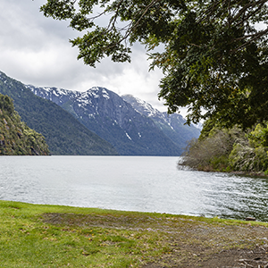 Orilla del Lago Frías encajonado entre laderas boscosas y cumbres con nieve.