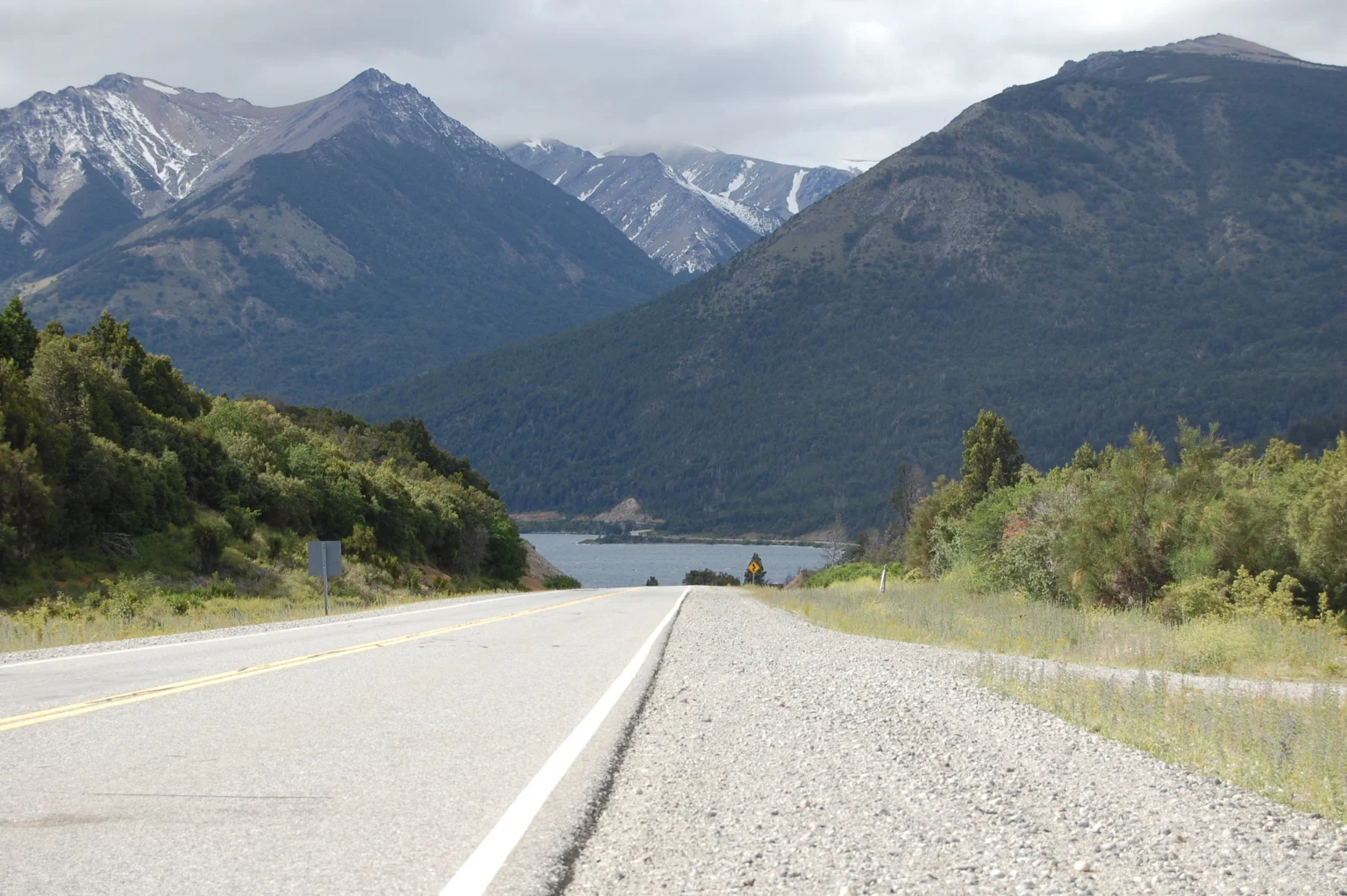 Ruta asfaltada bordeando el lago hacia cerros nevados, en el camino de Bariloche a Villa La Angostura.