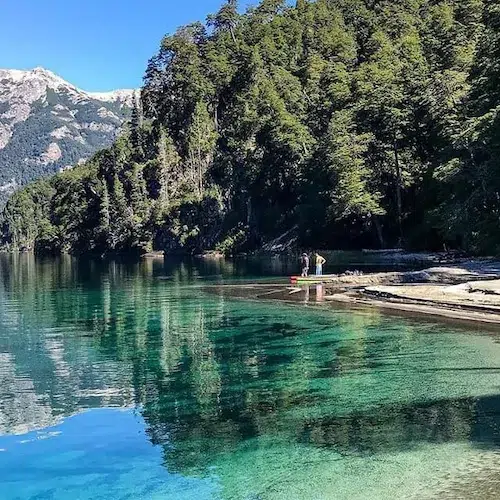 Playa y aguas turquesas del lago Espejo entre bosque andino y cerros nevados