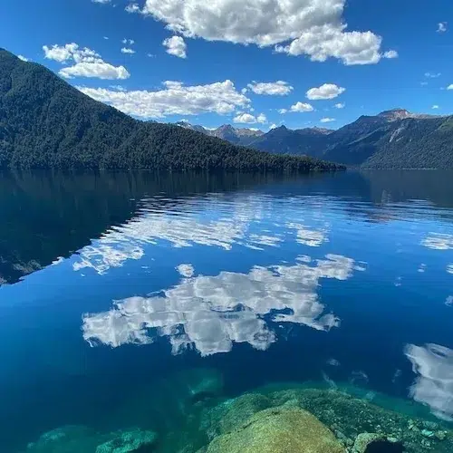 Aguas transparentes del lago Traful con nubes reflejadas y cerros boscosos