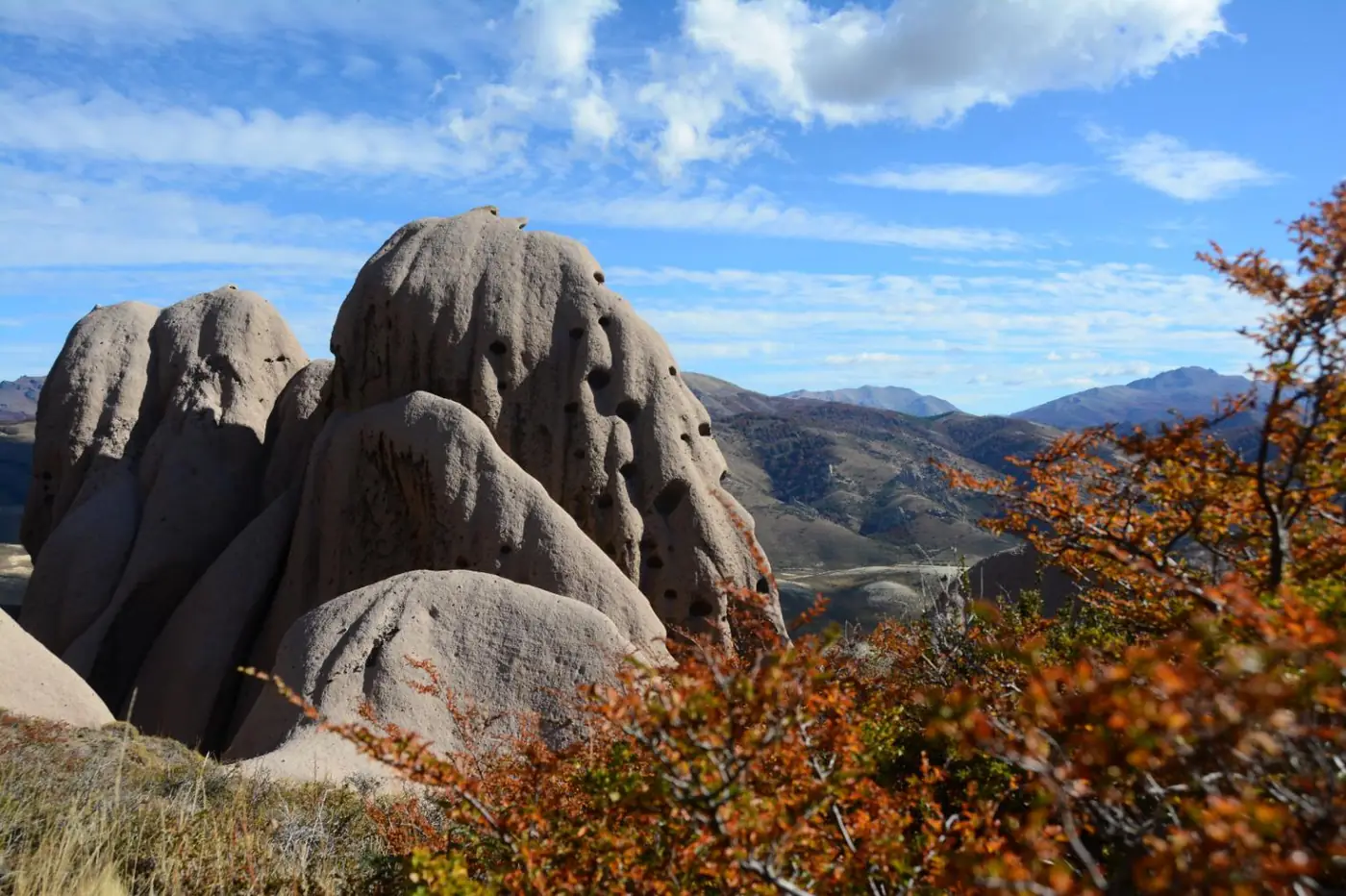 Hongos de piedra perforados por el viento, con ñires en colores de otoño y la cordillera al fondo.