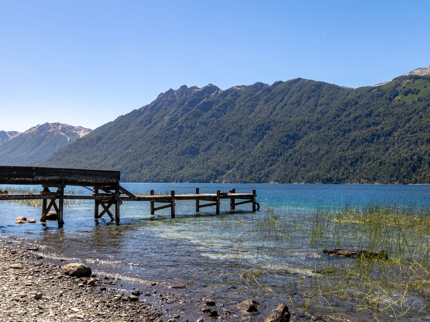 Muelle de madera sobre el Lago Correntoso con la cordillera boscosa al fondo.